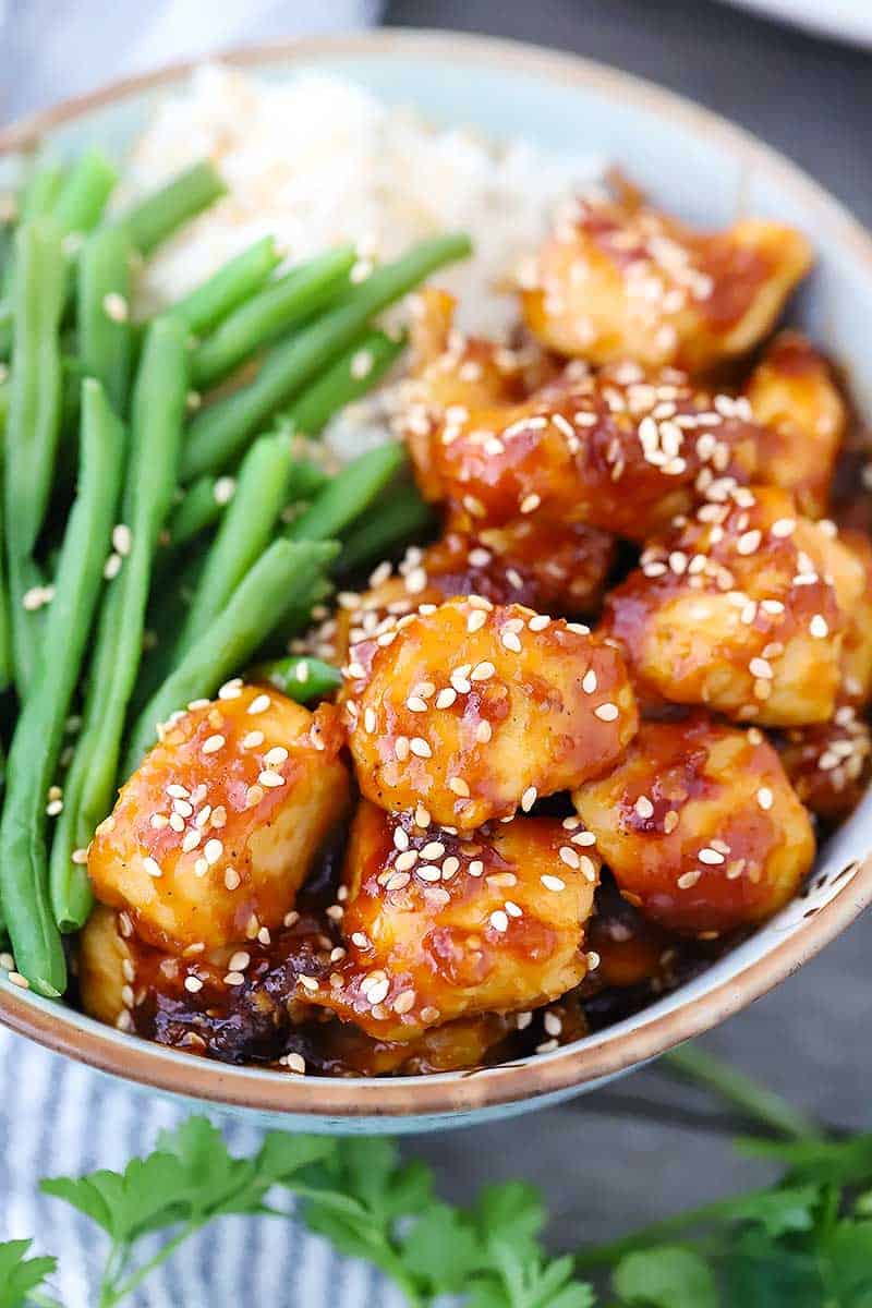 Close up photo of a bowl of sesame chicken garnished with sesame seeds.
