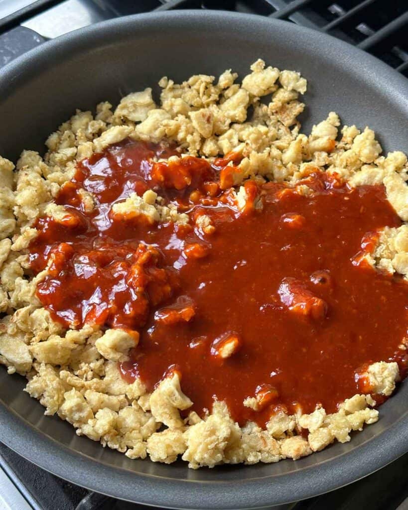 Adding gochujang sauce to crispy tofu in a skillet.