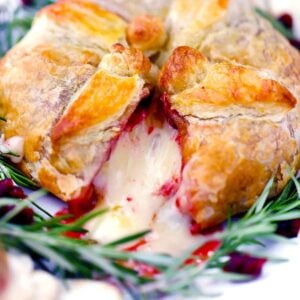 Square photo of baked brie en croute with cranberry sauce with a slice cut out.