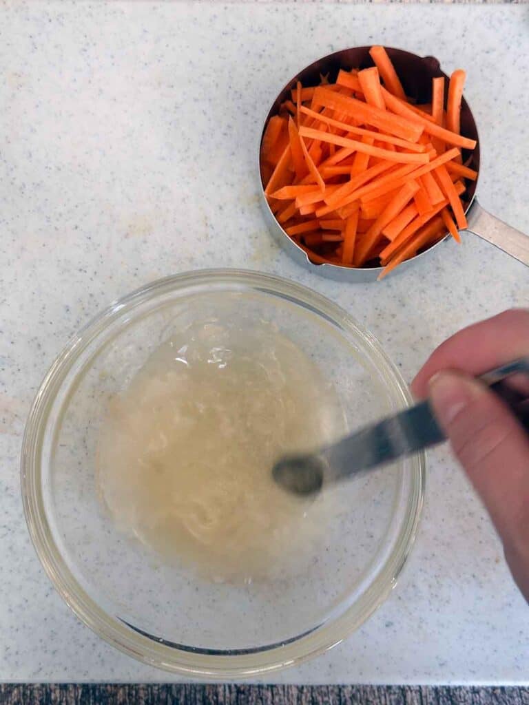 Mixing vinegar, sugar, and salt to make pickled carrots for Bánh Mì hot dogs.