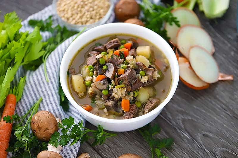 Horizontal photo of a white bowl of beef barley soup.