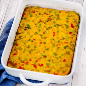 Square photo of a white baking dish with breakfast egg sausage casserole on a blue towel.