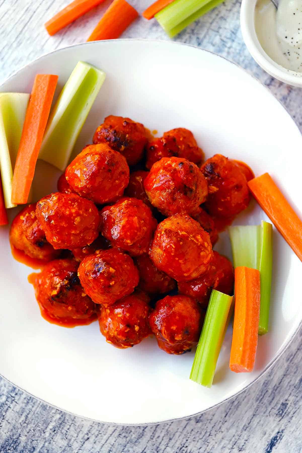 Overhead photo of a white plate with buffalo chicken meatballs, celery, and carrots on it.