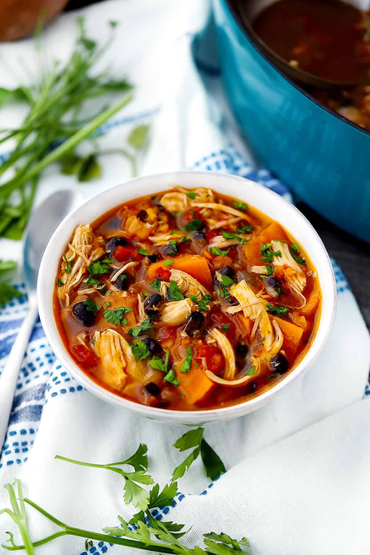 Chicken stew in a white bowl with parsley around it on a white towel.