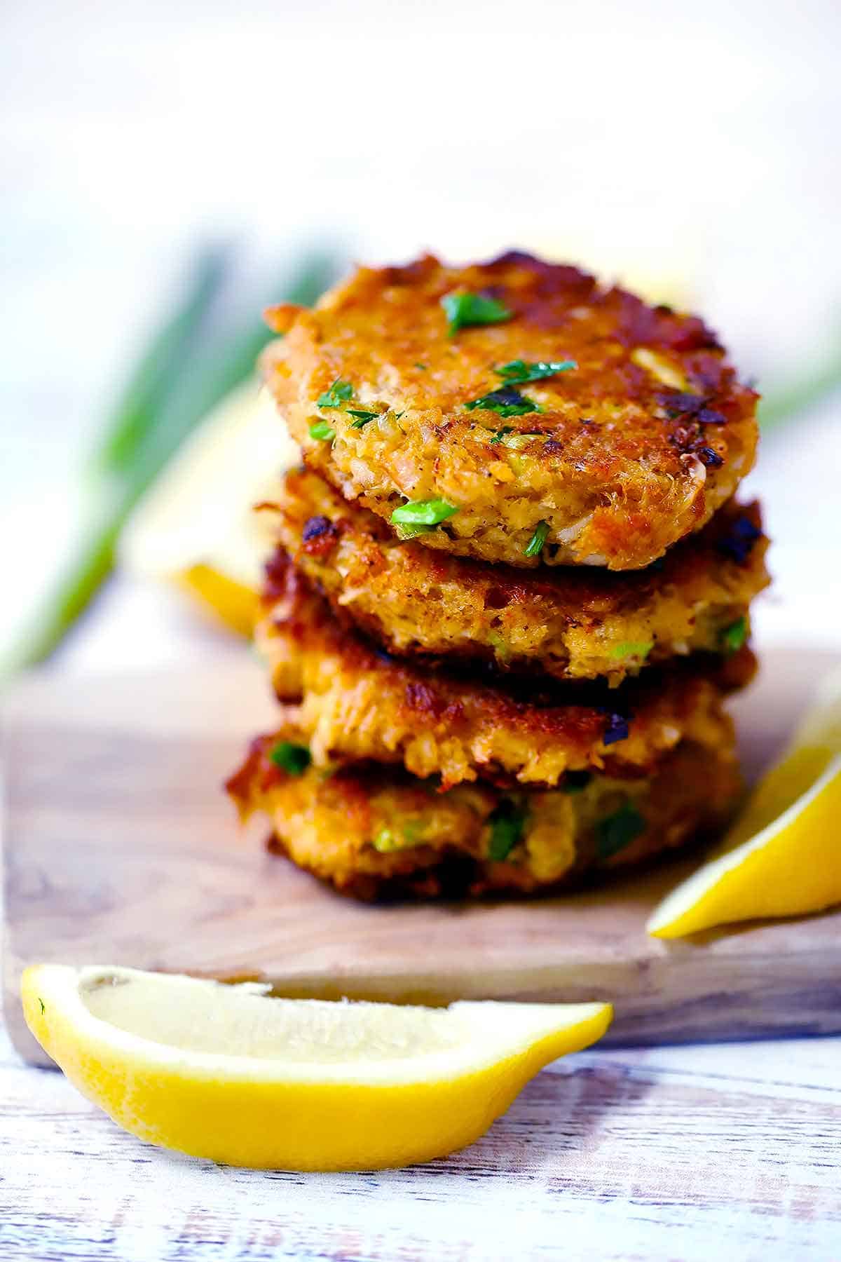 A stack of crab cake patties with fresh lemon wedges around it.