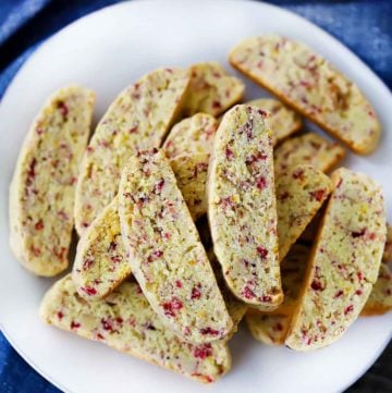 An overhead photo of cranberry orange biscotti on a white plate with a blue towel.