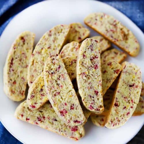 An overhead photo of cranberry orange biscotti on a white plate with a blue towel.