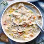 Square photo of creamy chicken and rice soup in a white bowl, overhead view, with a spoon.