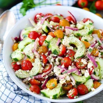 Cucumber and tomato salad with feta cheese in a bowl with a spoon next to it.