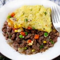 A close up photo of a white plate with shepherd's pie and a fork.