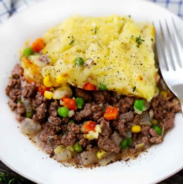 A close up photo of a white plate with shepherd's pie and a fork.