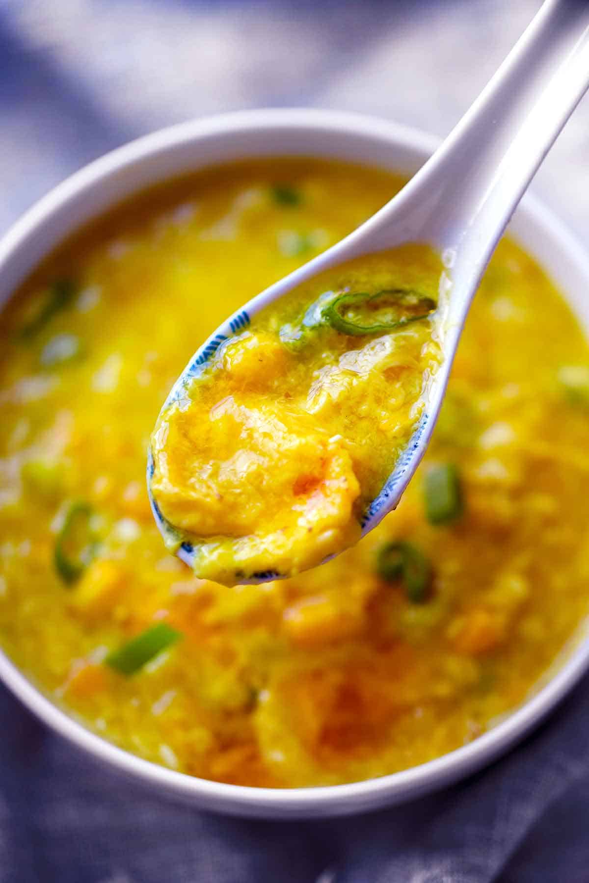 A spoonful of egg drop soup over a white bowl filled with it.