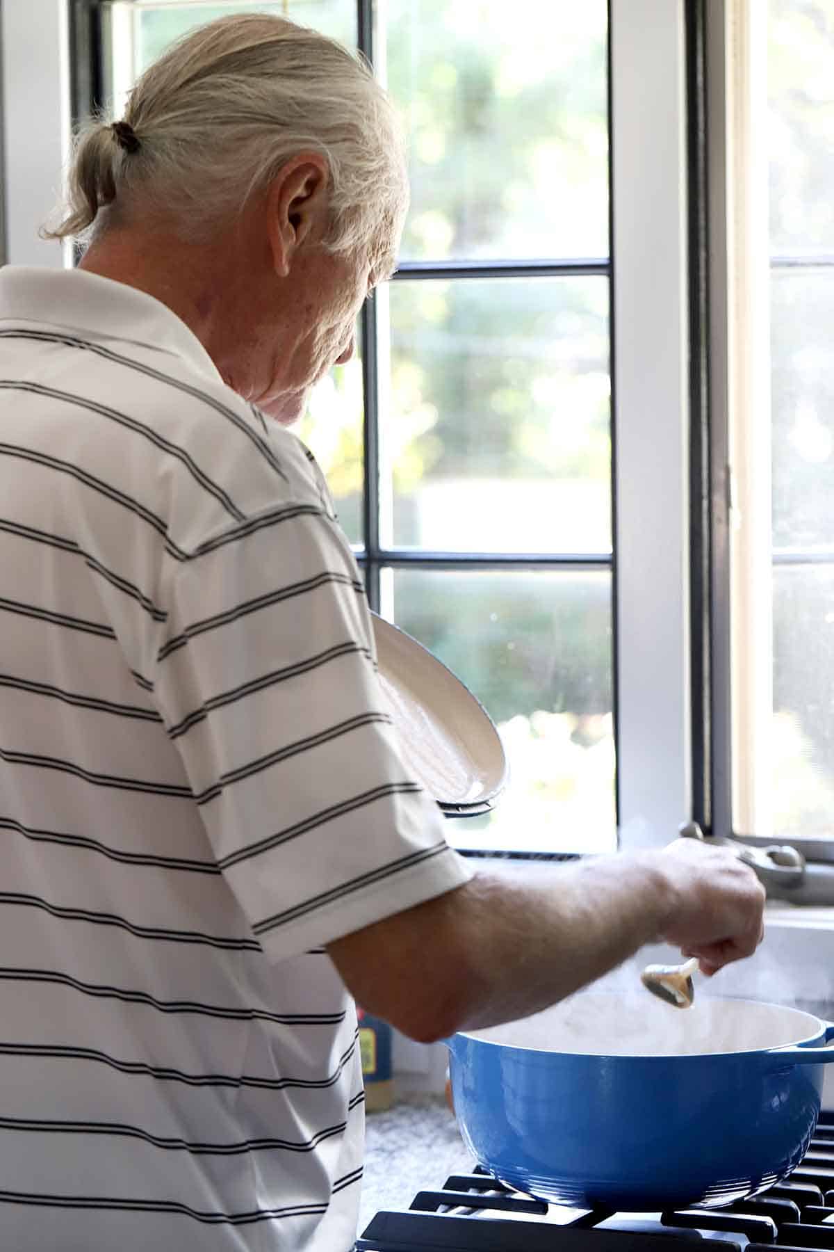 Man standing at stovetop stirring chowder in a Dutch Oven.