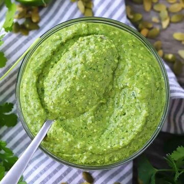Square photo of overhead view of bowl of avocado sauce with spoonful lifting out of it.
