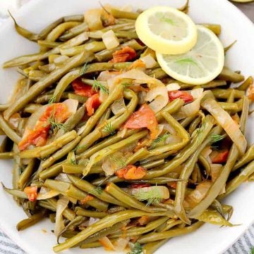 Overhead photo of Greek Green Beans with tomatoes and lemon in a white bowl.