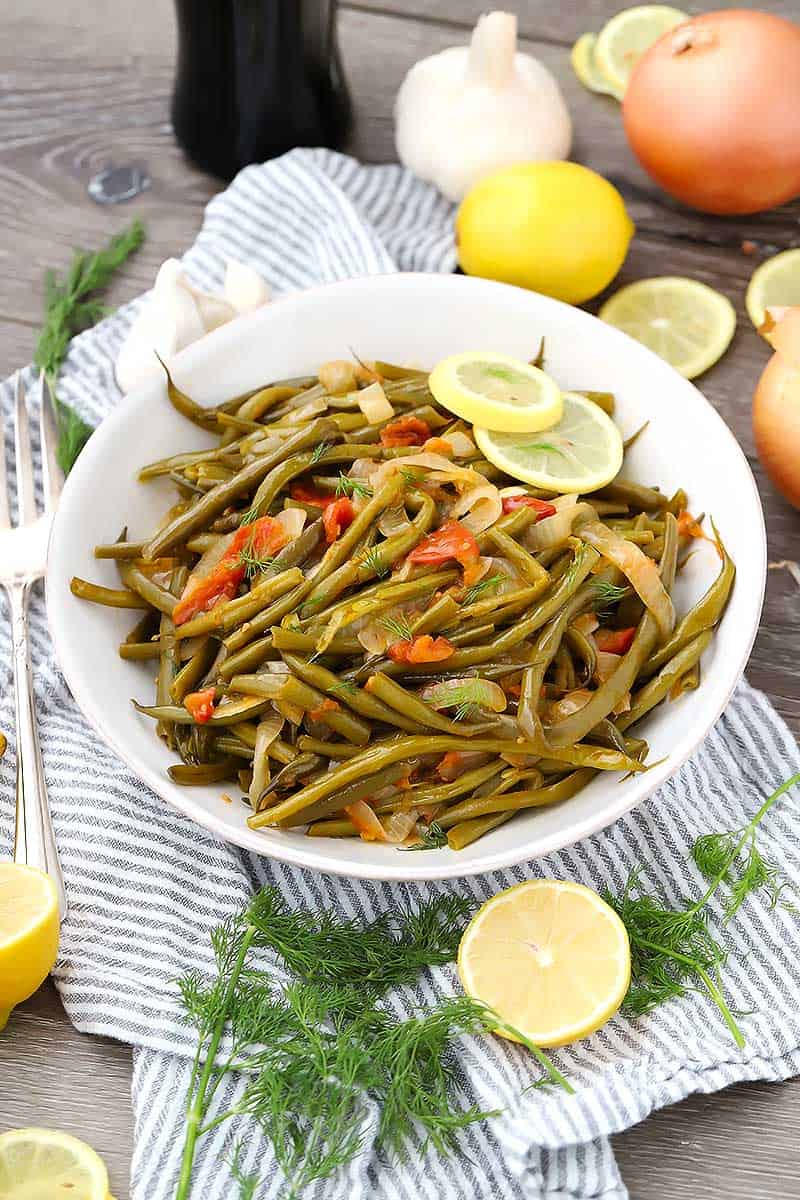Greek green beans, or fasolakia, in a white bowl with lemon slices.