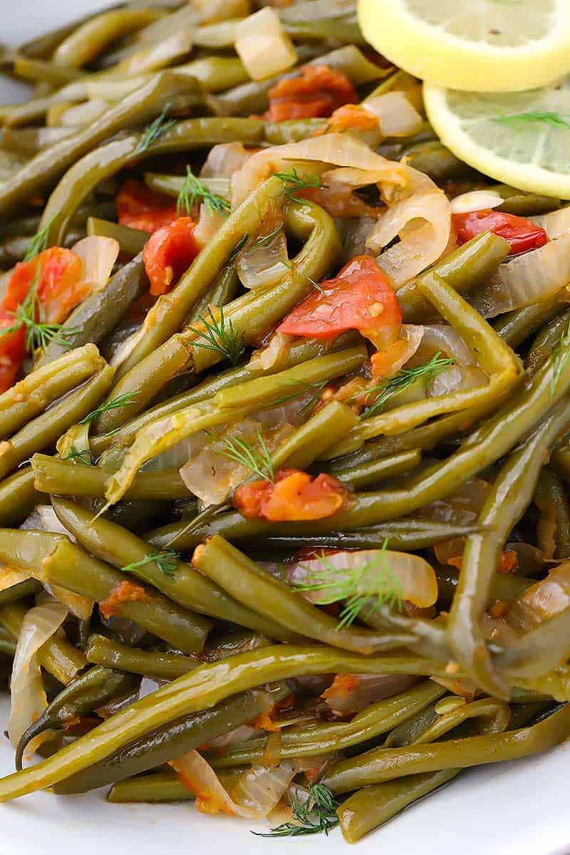 Close up photo of Greek Green Beans, or Fasolakia, with dill lemon and tomatoes.