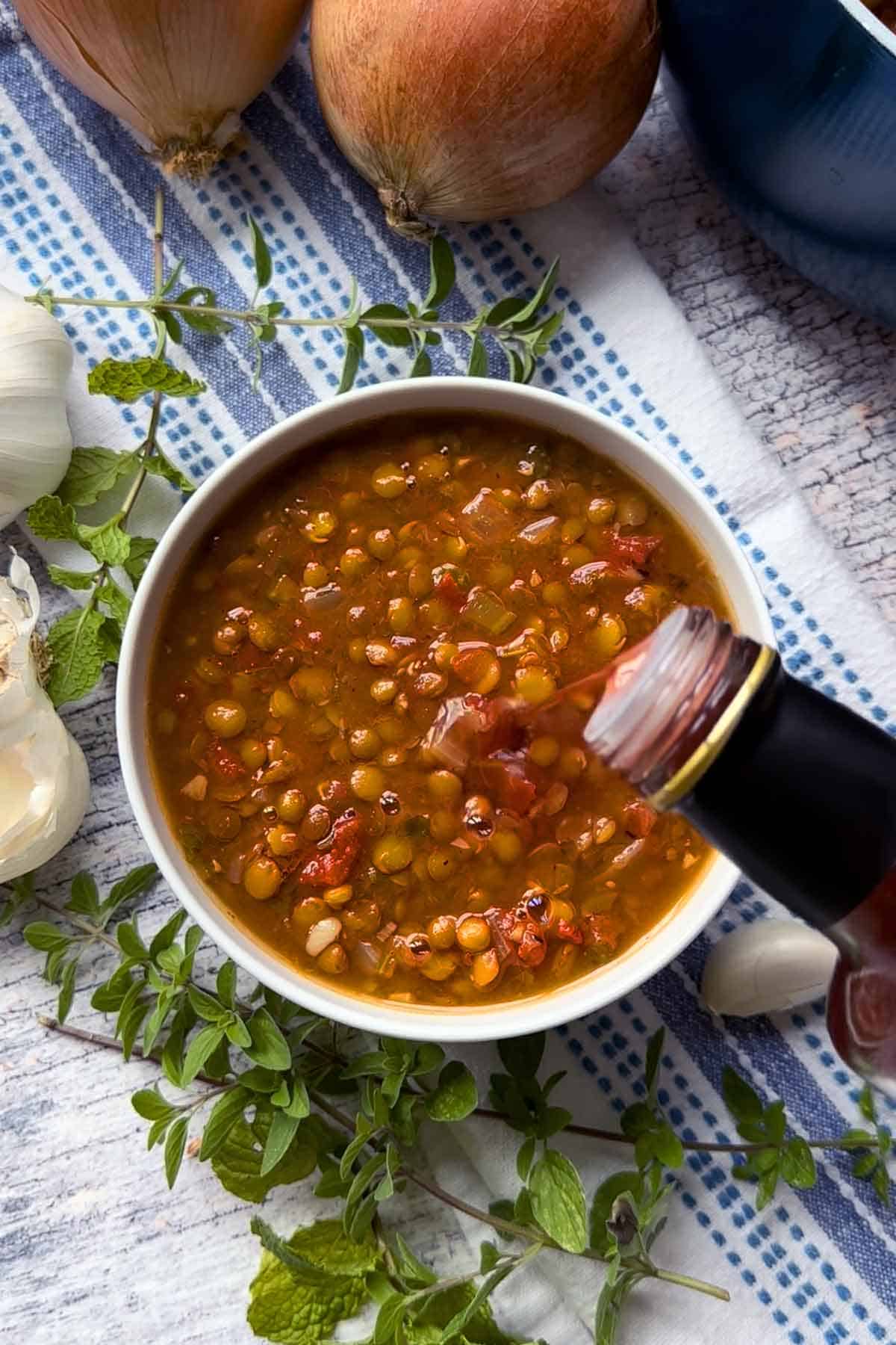 Showing drizzling red wine vinegar into a bowl of Greek lentil soup.
