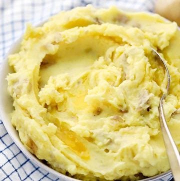 A bowl of homemade mashed potatoes with melted butter and a spoon.