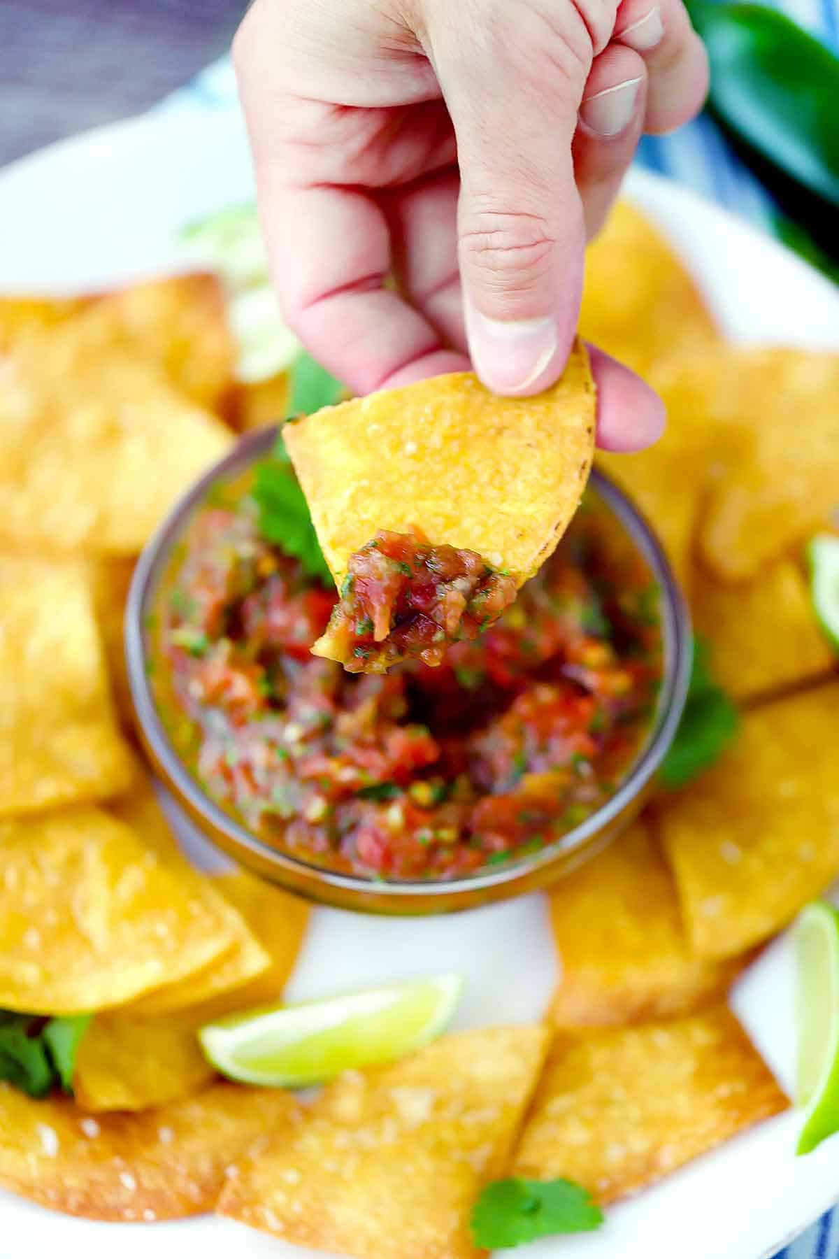 A hand dipping a homemade tortilla chip in salsa.