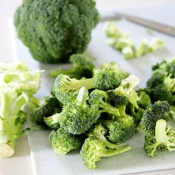 A head of broccoli cut up into florets on a cutting board.
