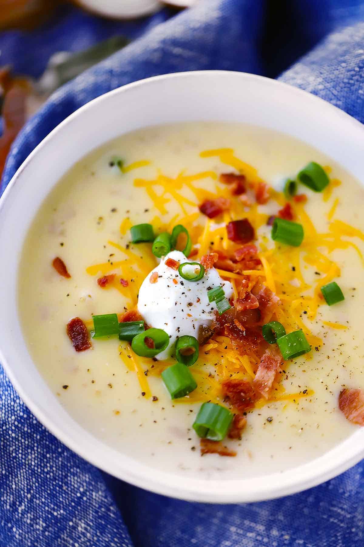A bowl of loaded baked potato soup topped with sour cream, cheese, green onion, and bacon.