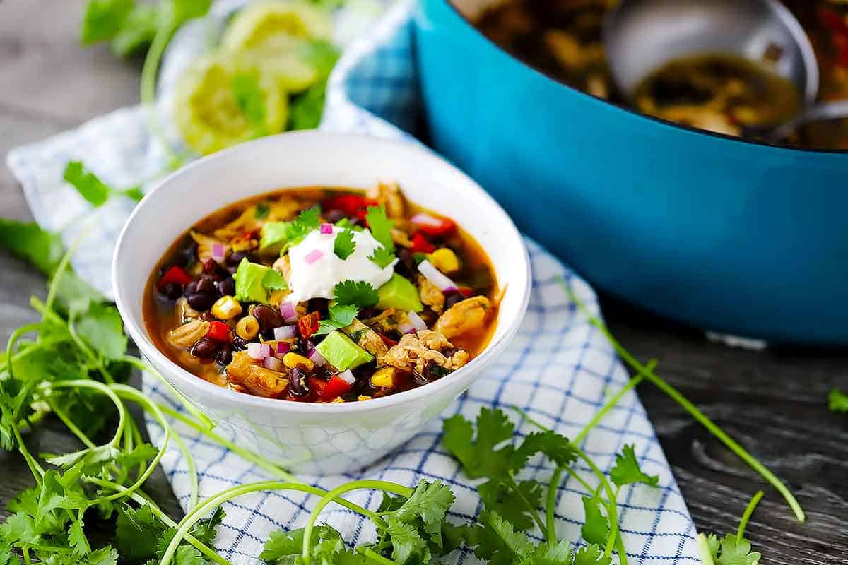 Horizontal image of a white bowl with turkey soup and a blue dutch oven in the background.