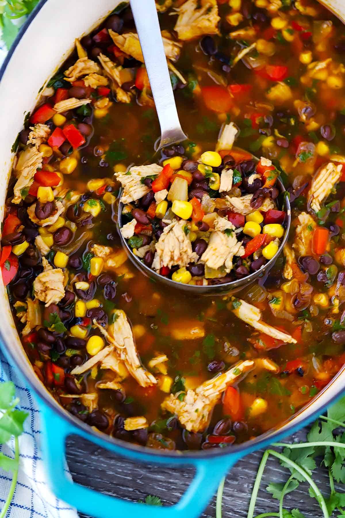 A ladle in a dutch oven with leftover turkey soup with black beans and corn in it.