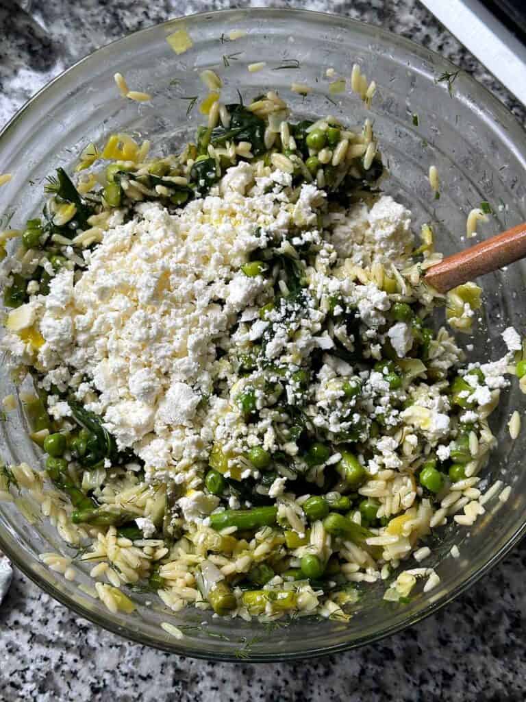 Stirring crumbled feta cheese into orzo with veggies.