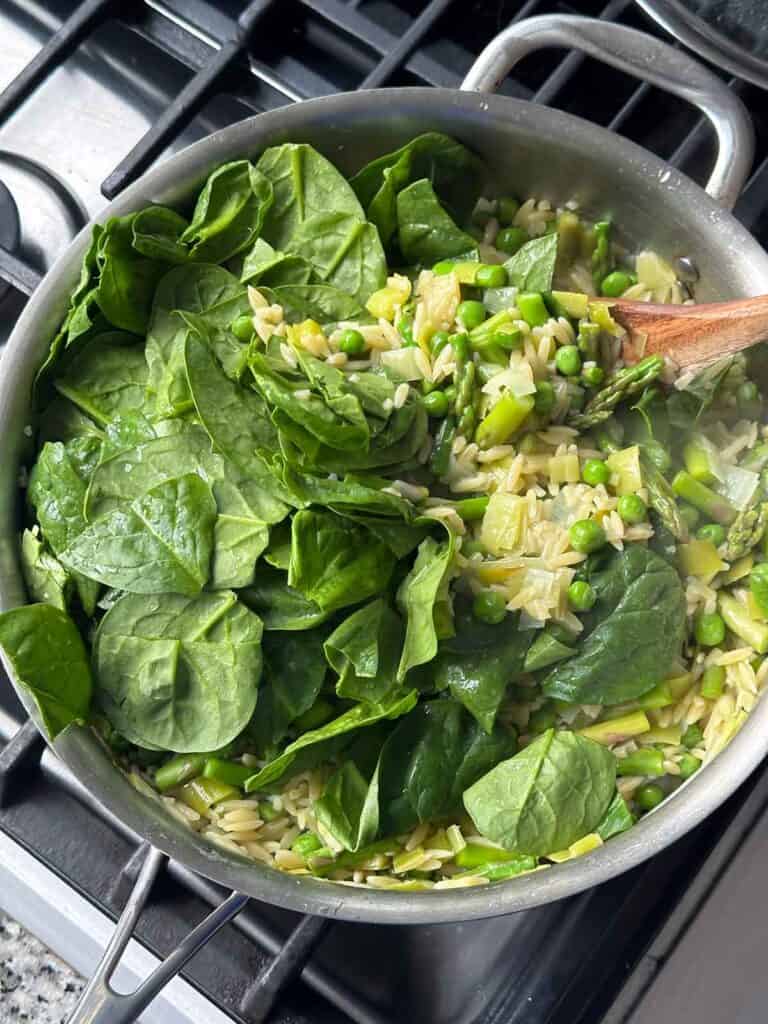 Adding baby spinach to warm orzo with veggies in a skillet so it wilts in.
