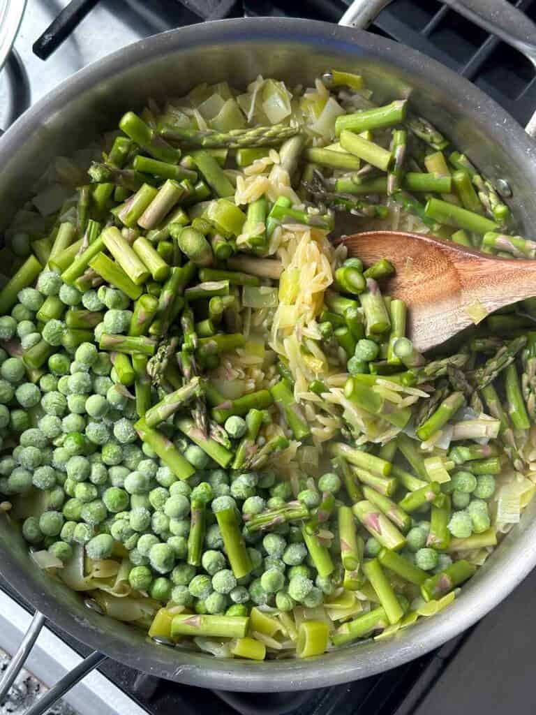 Adding asparagus and frozen peas to orzo in a skillet.