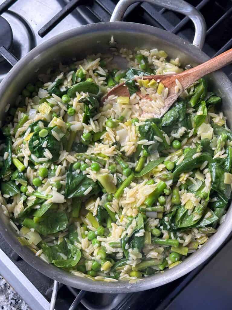 Orzo with spring vegetables in a skillet with wilted spinach.