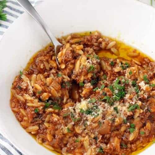 Close up bord's eye view of orzo and ground beef (manestra) in a white bowl, with spoon inside bowl.