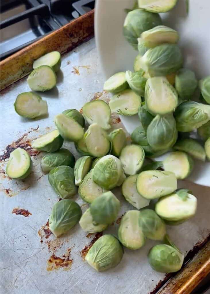 Adding Brussels sprouts to a baking sheet with bacon grease.