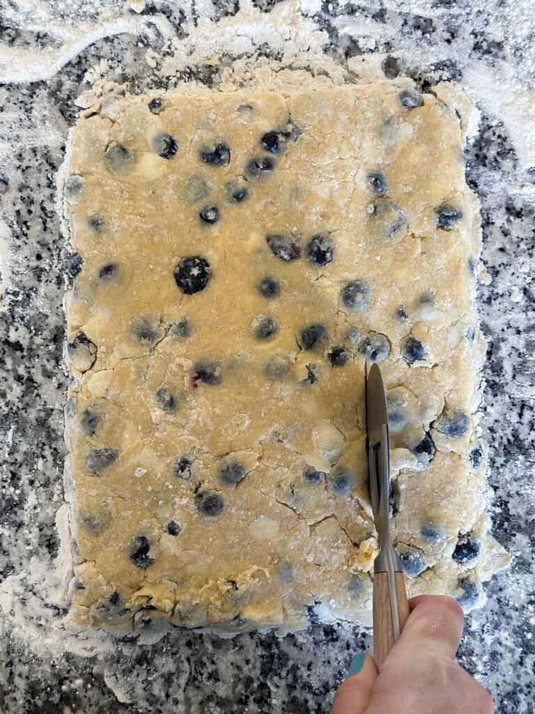 Cutting blueberry scone dough into mini triangles using a pizza roller.