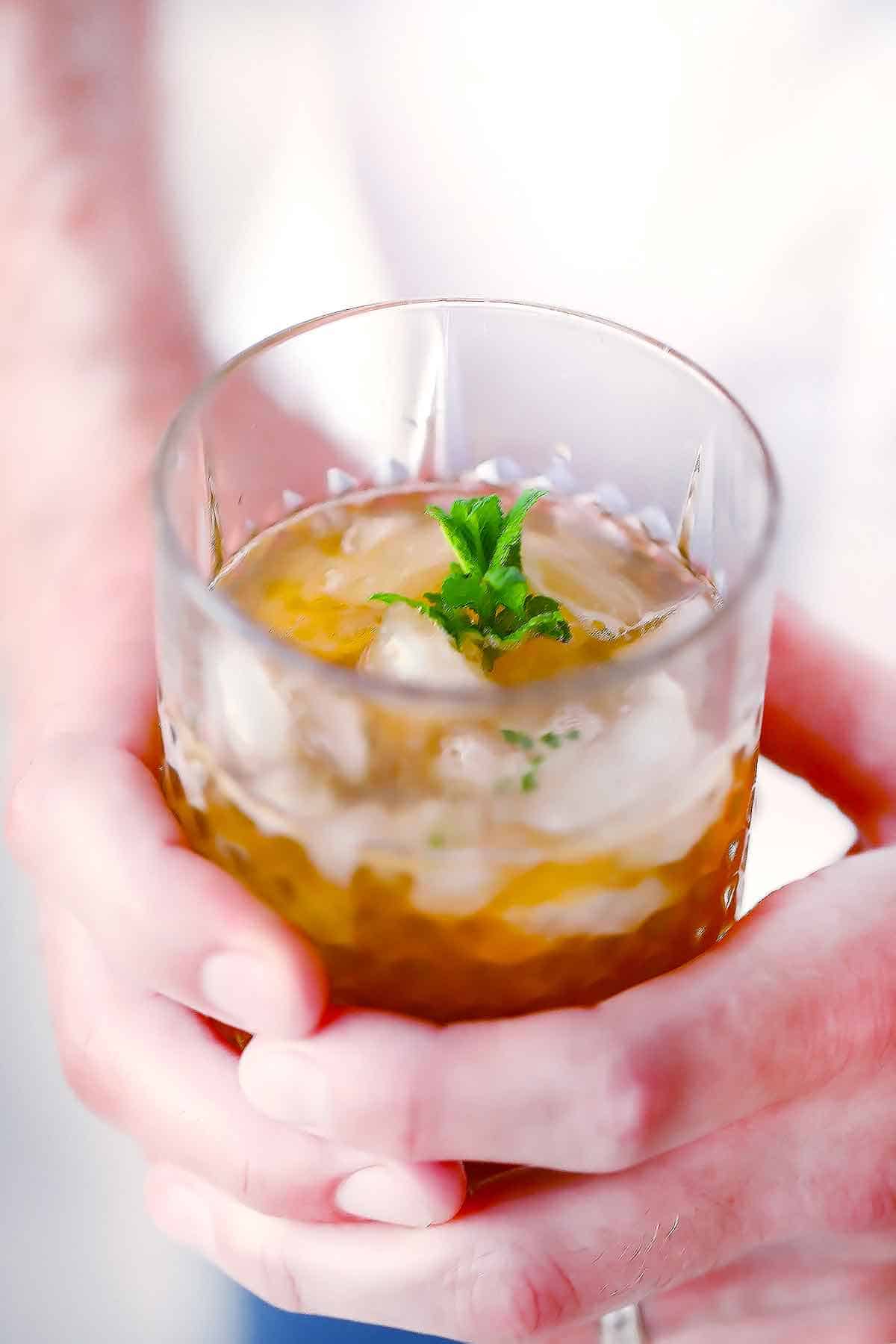 Hands holding a mint julep in an old fashioned glass.