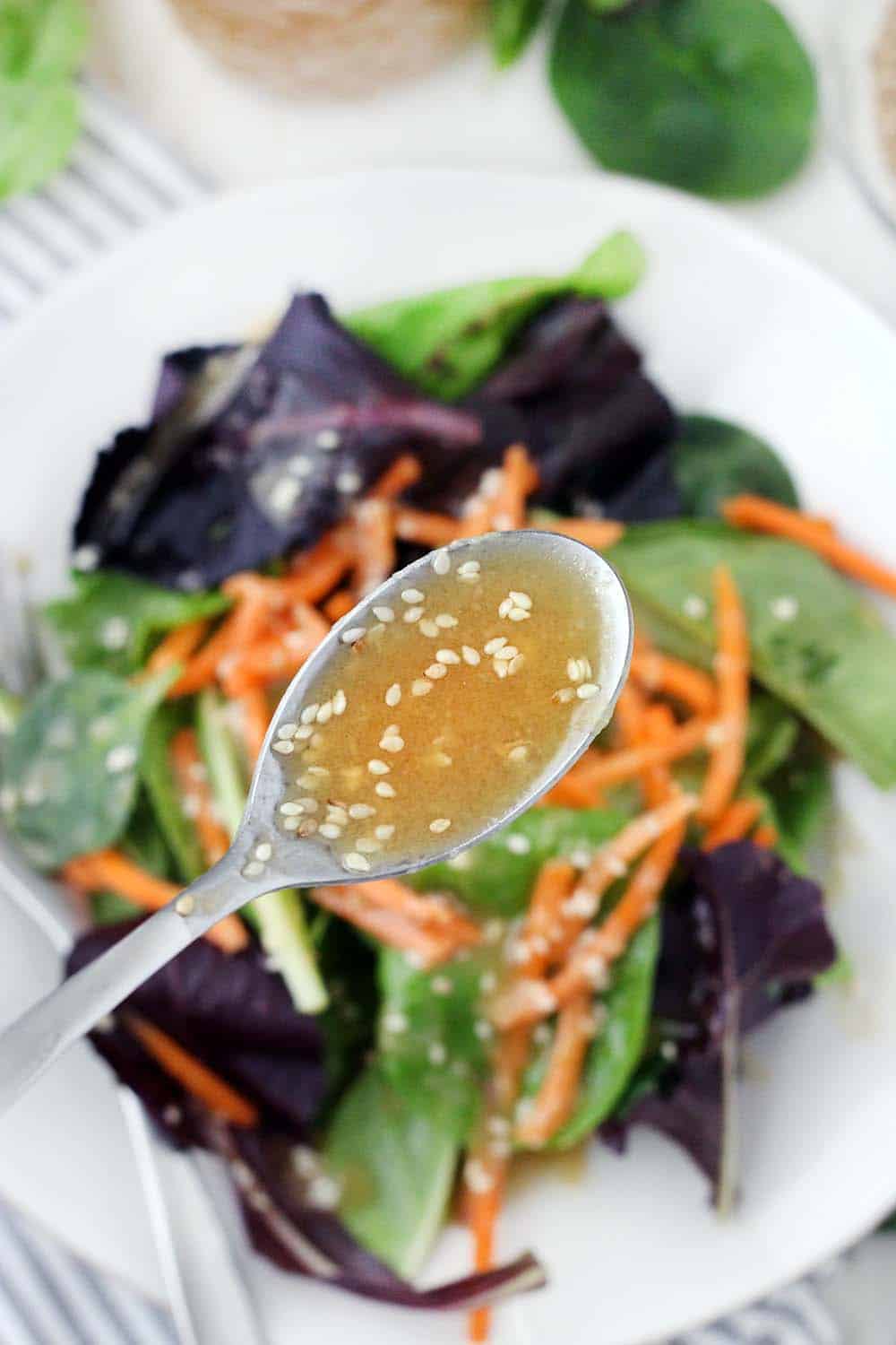Spoon filled with peanut dressing raised above bowl of fresh lettuce leaves and shredded carrots.