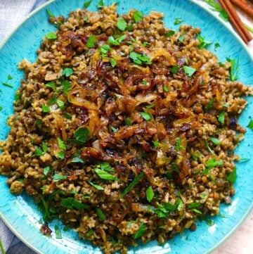 Square cropped overhead photo of Mujadara (lentils, rice, and caramelized onions) on a blue plate garnished with parsley.
