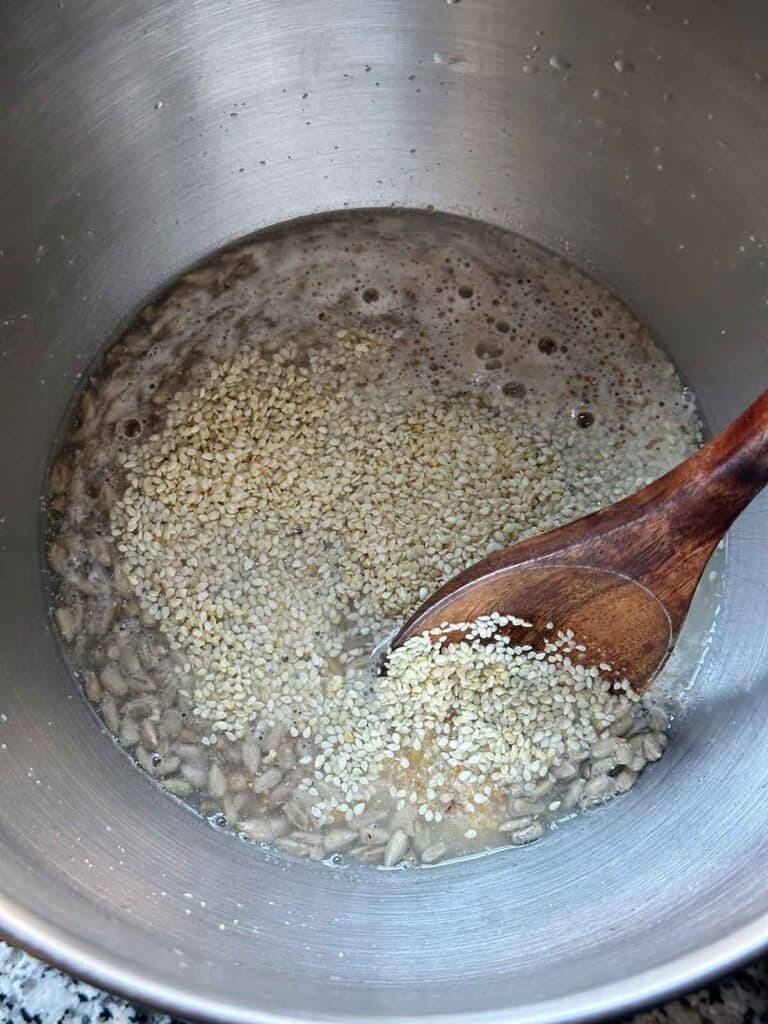 Mixing a 10 grain hot cereal mix and sesame, sunflower, and flax seeds into a warm water and yeast mixture to make homemade multigrain bread.