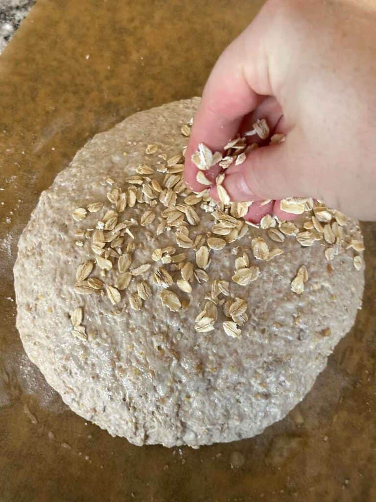 Sprinkling the top of a no knead multigrain bread loaf with rolled oats.