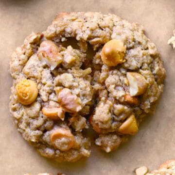 Close up overhead photo of an oatmeal butterscotch cookie with walnuts broken in half to show texture on brown parchment paper.