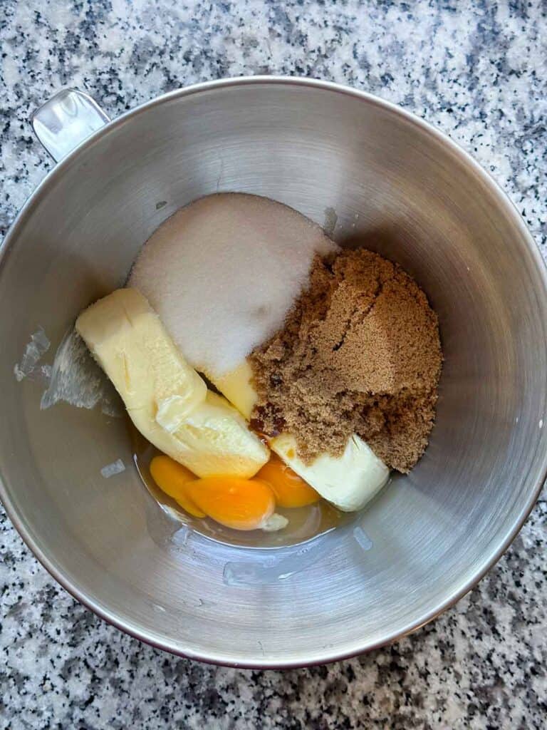 A mixing bowl showing butter, brown sugar, white sugar, and eggs, before being beaten together for cookie dough.