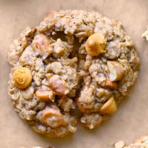 A close up top down photo of an oatmeal butterscotch cookie on brown parchment paper, broken in half to show texture.