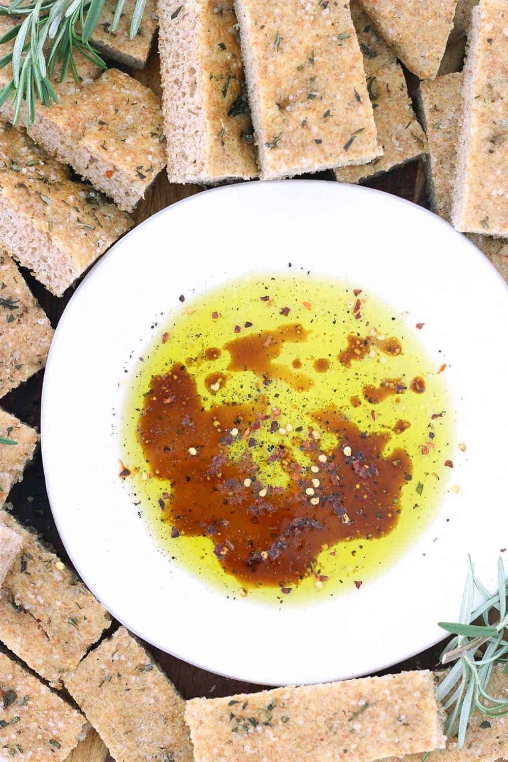 Close up photo of live oil, balsamic vinegar, and herbs in a shallow white bowl surrounded by pita chips.