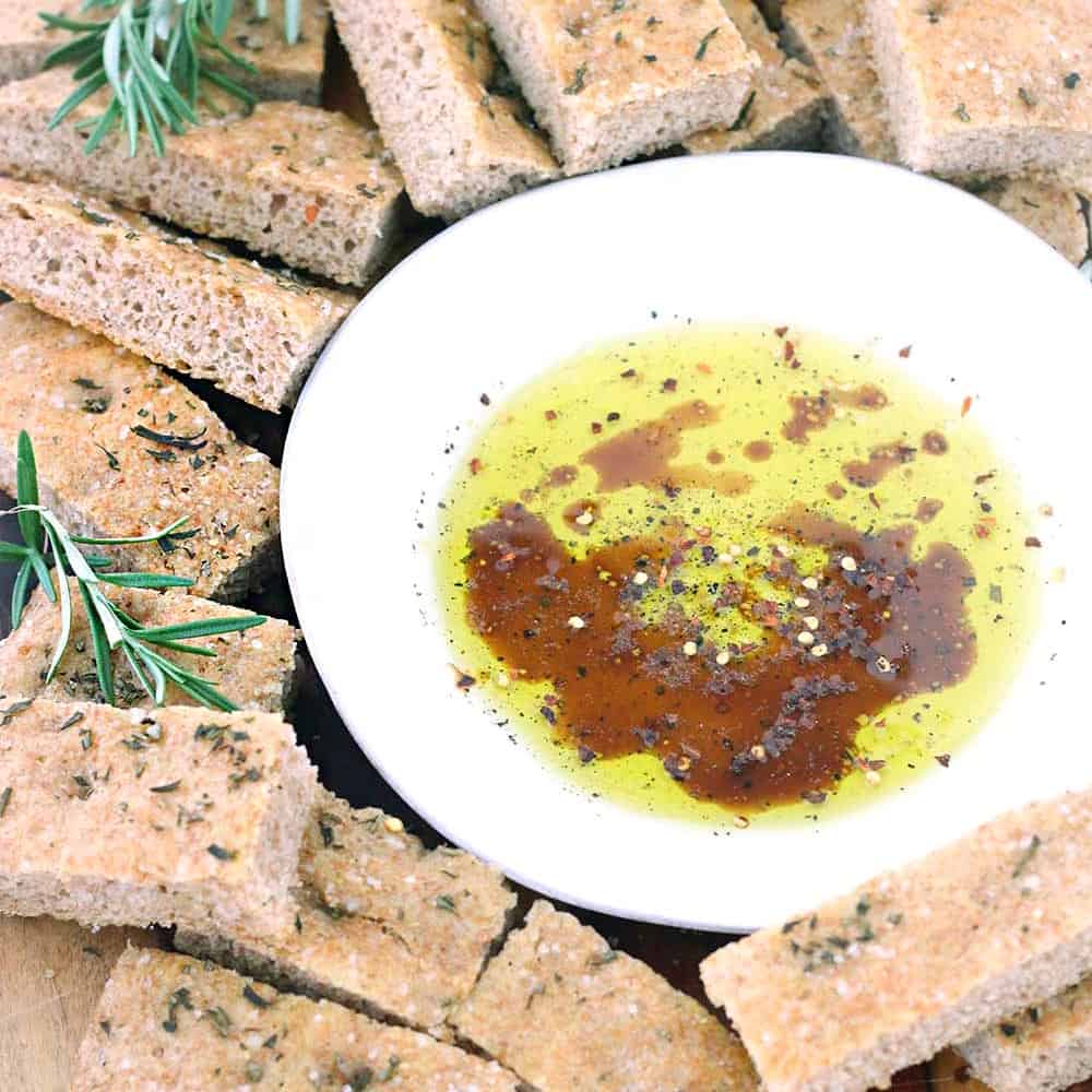 Olive oil, balsamic vinegar, and herbs in a shallow white bowl surrounded by pita chips.