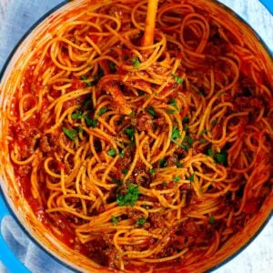 Square photo of an overhead view of a pot with spaghetti and meat sauce garnished with parsley in a blue Dutch oven.
