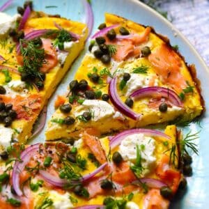 Square photo of an open faced omelette slice topped with smoked salmon, cream cheese, capers, and red onions.