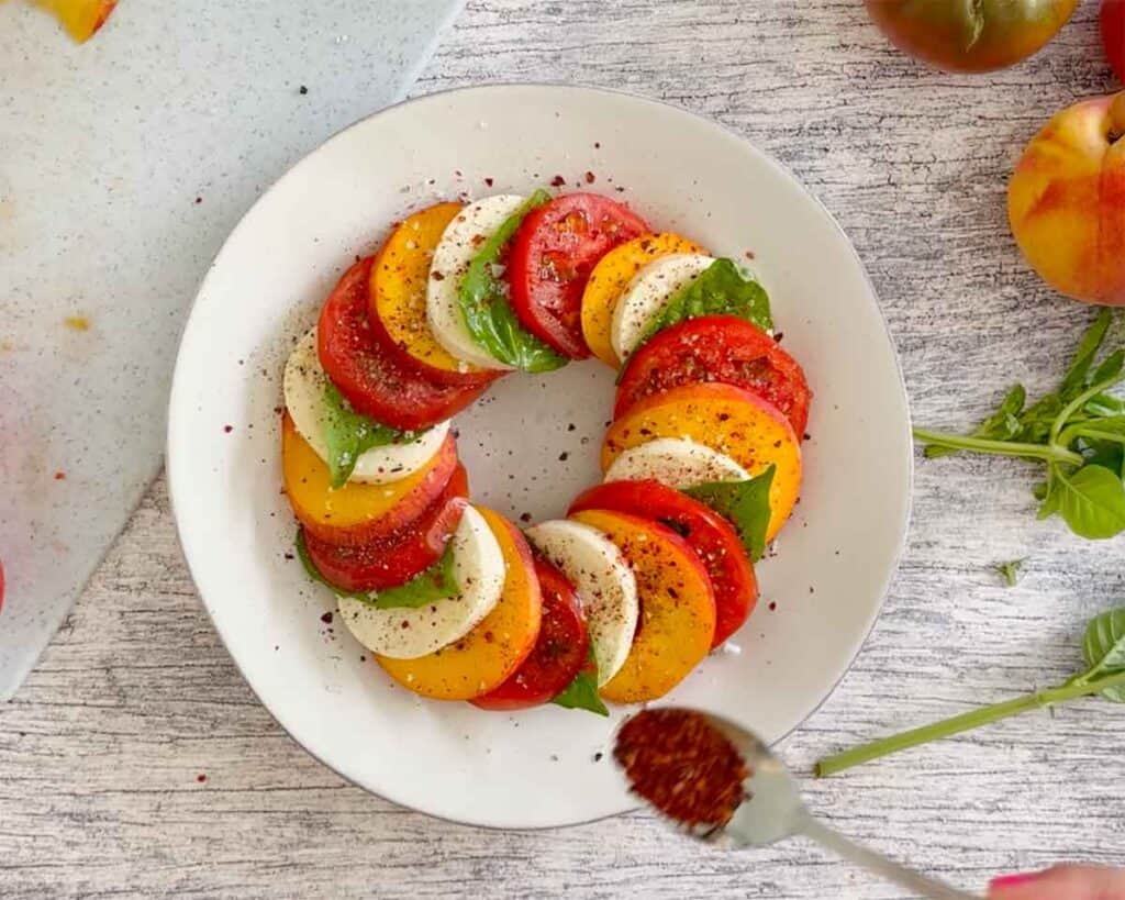 Sprinkling a peach caprese salad with Aleppo pepper.