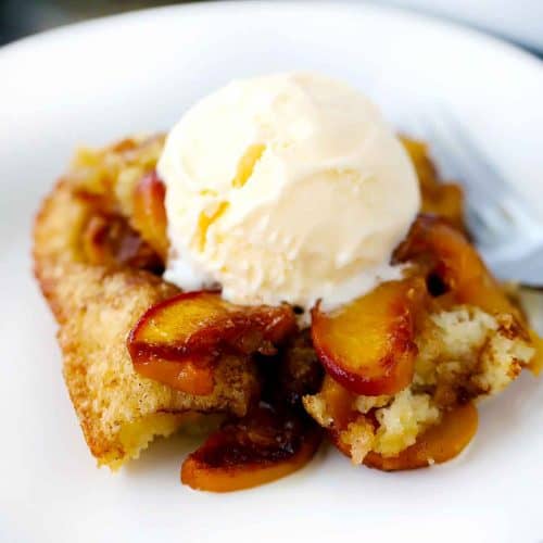 Close up photo of old-fashioned peach cobbler with vanilla ice cream melting on top.