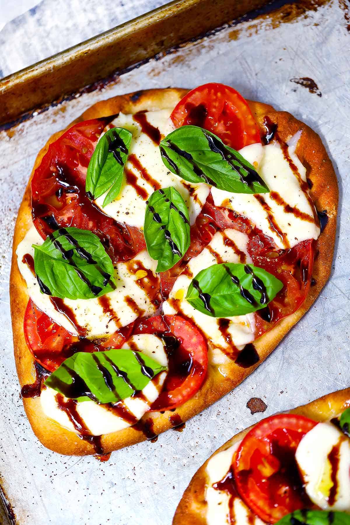 Overhead photo of a caprese pizza on naan bread with fresh mozzarella, tomatoes, fresh basil, and balsamic.
